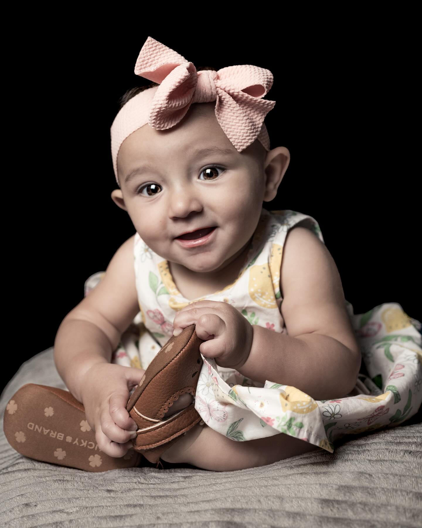 Studio baby portrait holding a shoe against a dark background